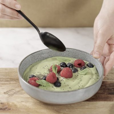 Green smoothie bowl con latte di mandorla, avocado e menta, guarnito con frutti di bosco e semi di chia
